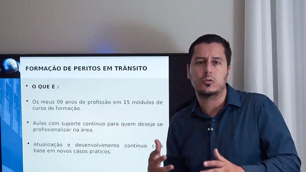 A imagem contém no primeiro plano o professor André Bittencourt, de camisa azul, gesticulando com as mãos, dando uma explicação sobre o curso online de Perícia em Acidentes de Trânsito. Ao fundo da imagem tem uma televisão mostrando algumas informações sobre o curso.